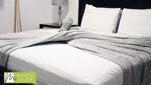 A neatly made bed with white linens and a grey blanket, a bedside lamp, and a wooden rack with clothes. - Mystic River Retreat | 3BR/2BA•Pool - Jacuzzi - Beverly Hills, Guaynabo, Guaynabo, Puerto Rico (Guaynabo)
