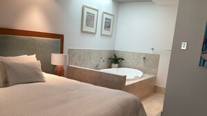 Hotellihuone, jossa on suuri sänky, kylpyammeella varustettu kylpyhuone ja kaksi kehystettyä kuvaa seinällä.