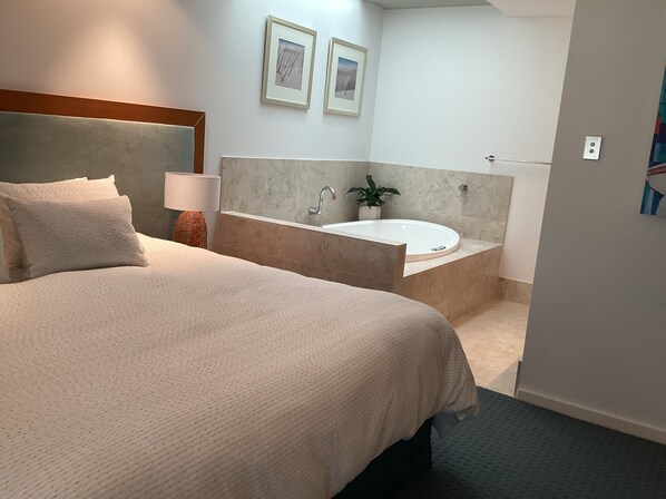 Una habitación de hotel con una cama grande, un baño con bañera y dos cuadros en la pared.