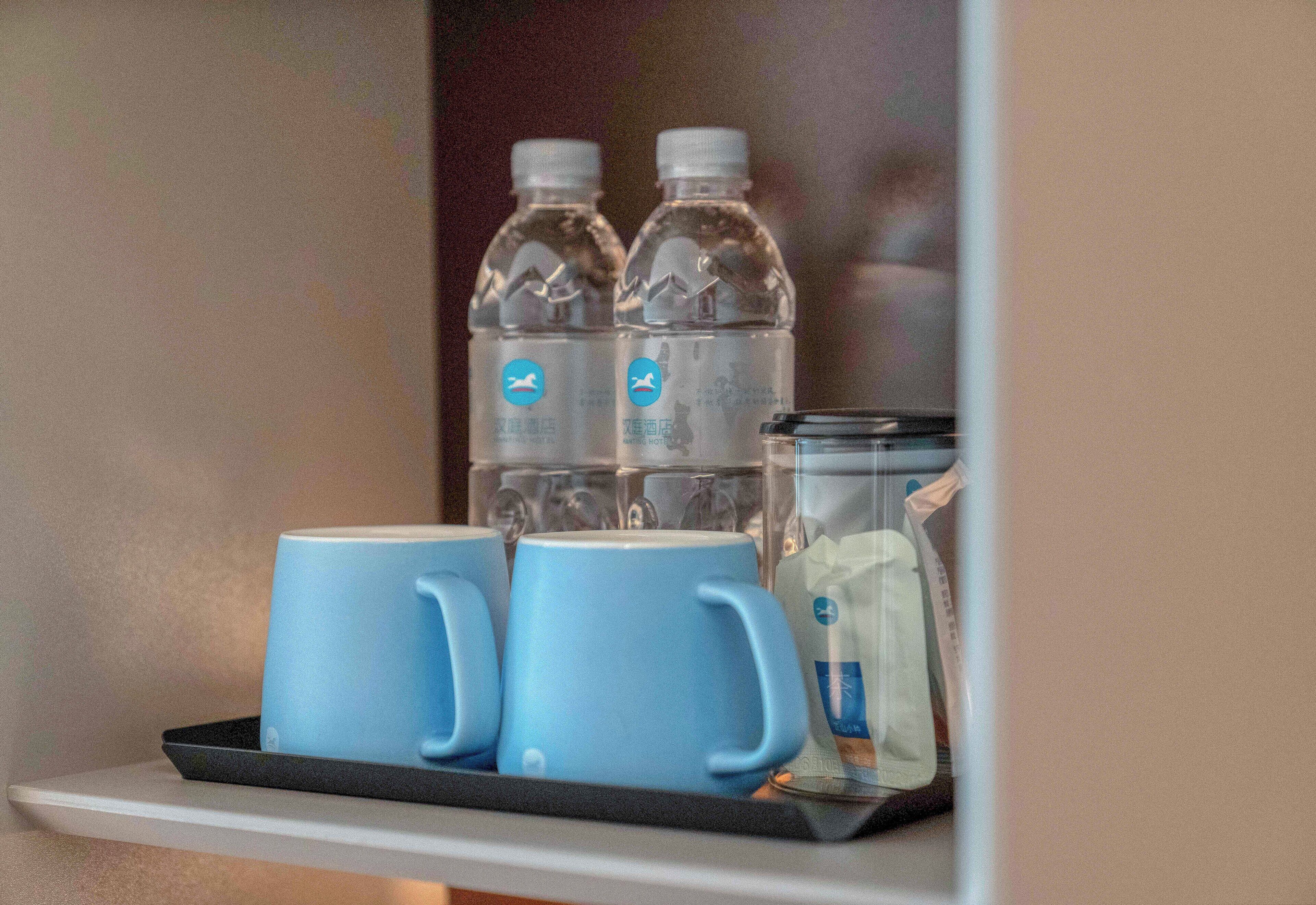En hylla med två vattenflaskor, tre blå muggar och en glasbehållare med ett tepåse i.