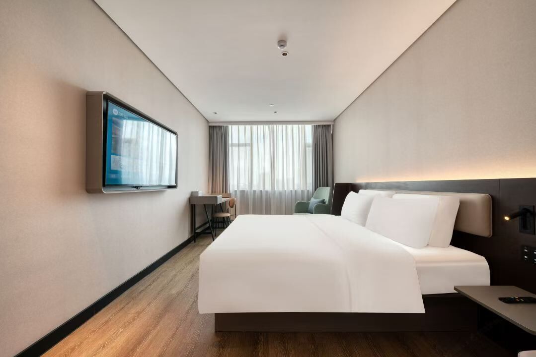 Una habitación de hotel moderna con una cama grande, un televisor de pantalla plana montado en la pared, un escritorio con una silla y una ventana con cortinas.