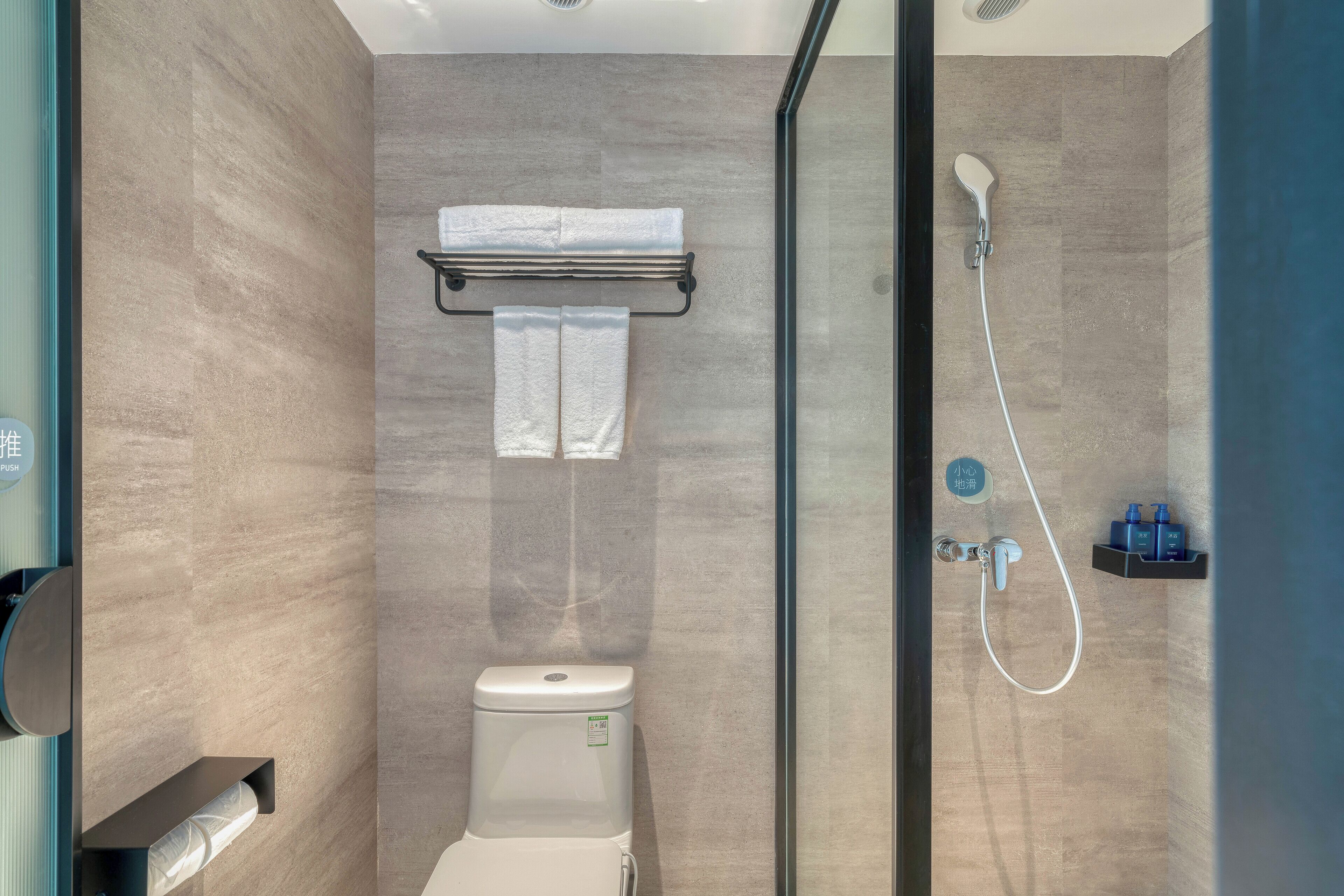 Un baño moderno con inodoro, toallero, cabina de ducha con mampara de vidrio y un estante pequeño con artículos de aseo.