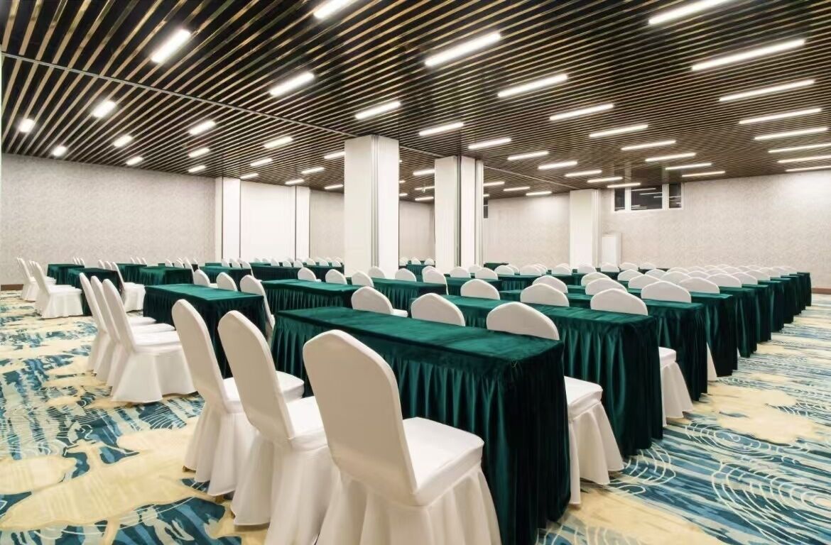 Une salle de conférence avec des rangées de tables et de chaises, une moquette à motifs et un design de plafond moderne.