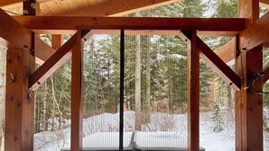 A wooden cabin with a screened porch overlooking a snowy landscape.
