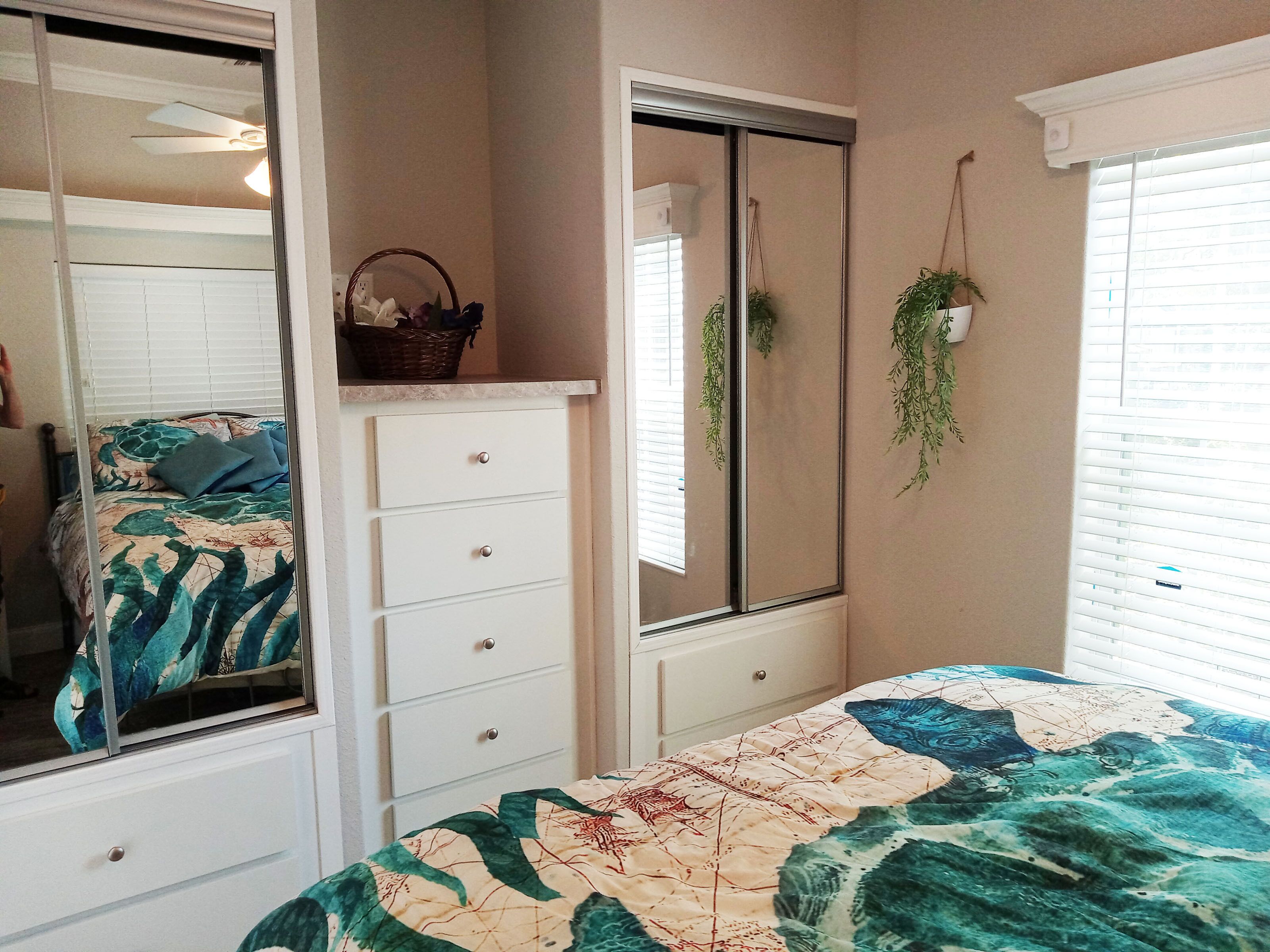 A bedroom with a bed, a dresser, a mirror, and a window with blinds.