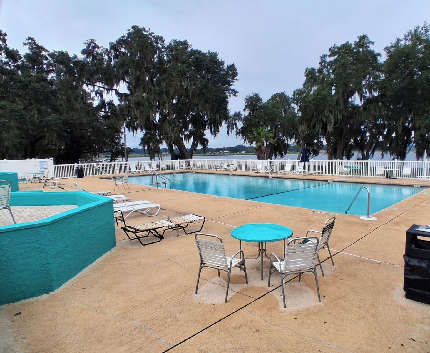 Una piscina con sillones de descanso y una mesa, rodeada de árboles.