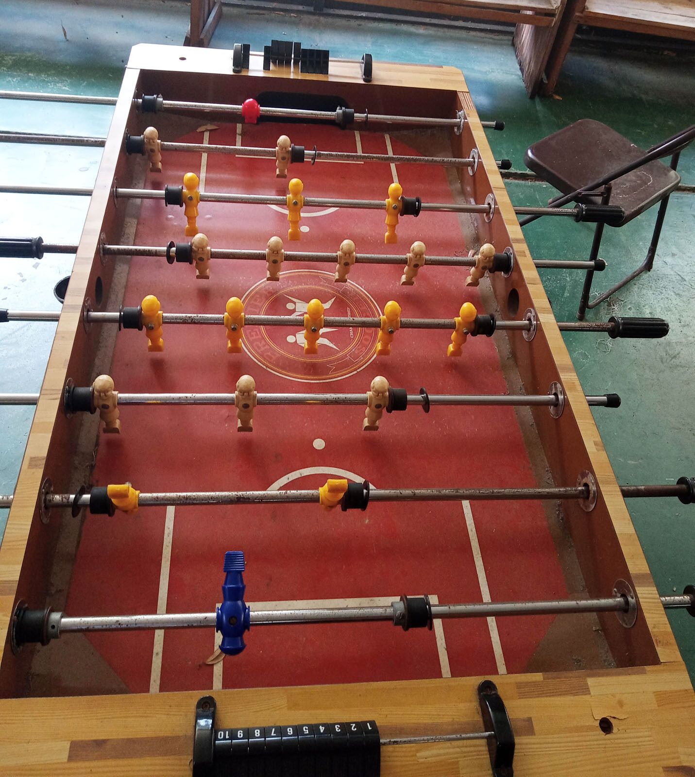 A foosball table with a red playing surface and multiple rods with figures.