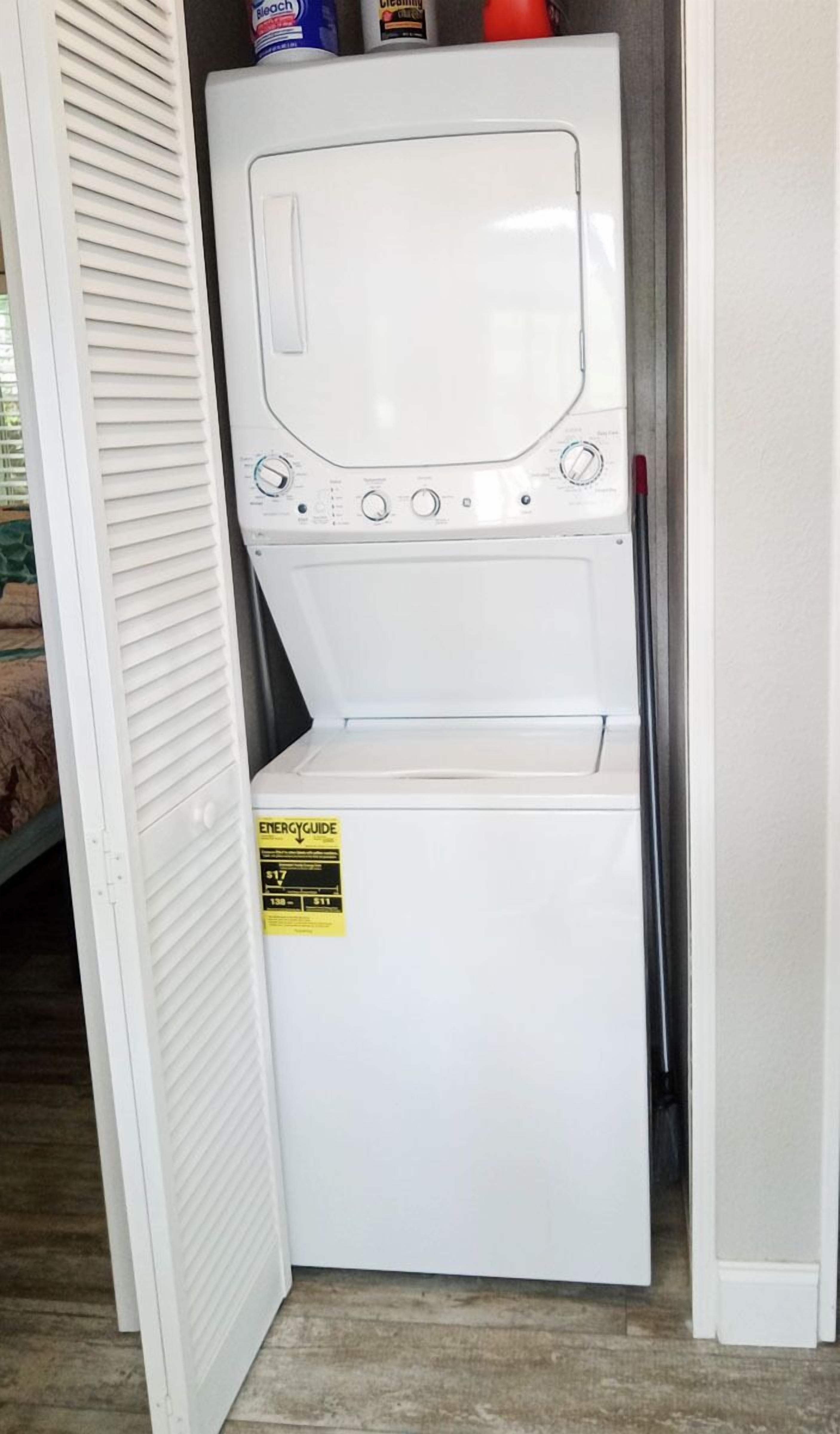 A compact washer and dryer unit with a control panel, a yellow energy efficiency label, and a red cleaning product on top.