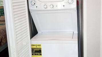 A compact washer and dryer unit with a control panel, a yellow energy efficiency label, and a red cleaning product on top.