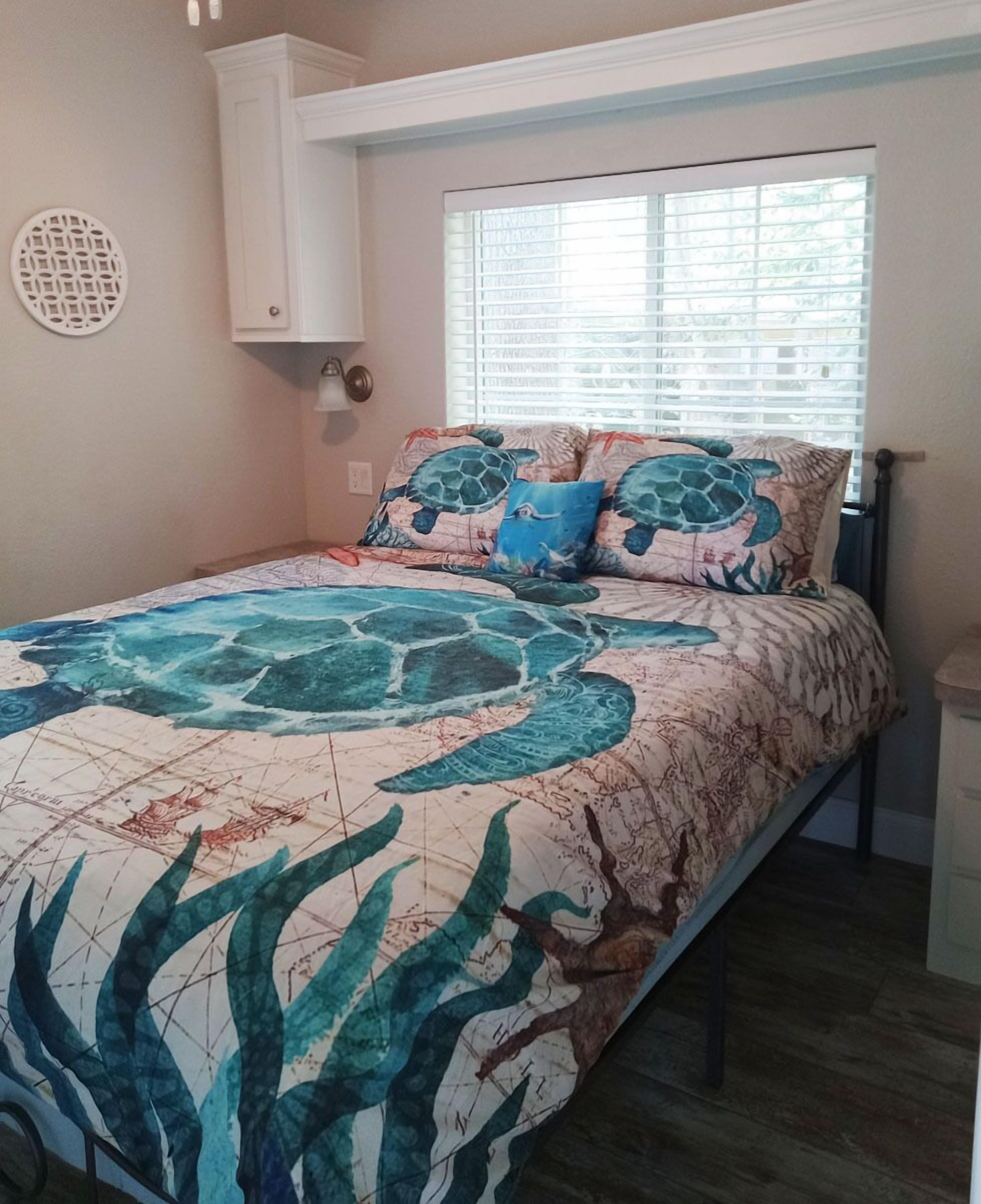 A bedroom with a bed, a window with blinds, a white cabinet, and a wall decoration.