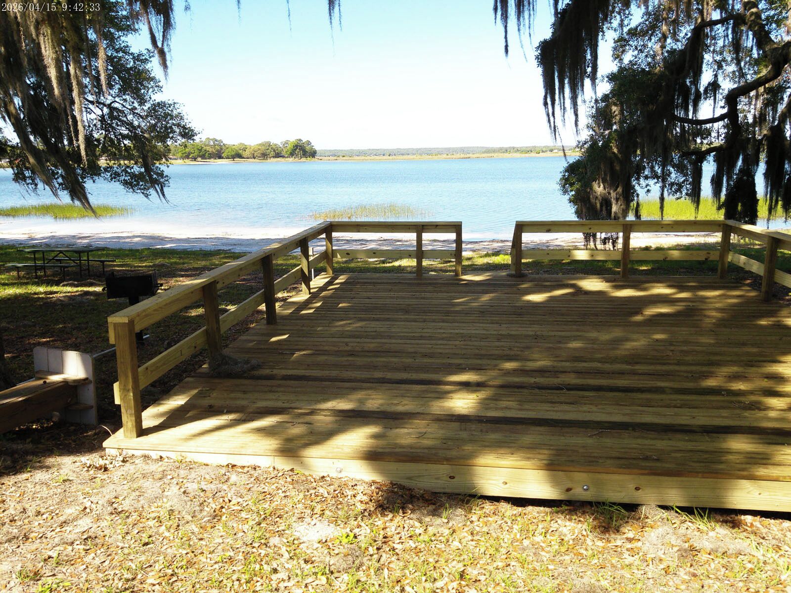 Una terraza de madera que da a un lago, con una mesa de picnic y zona de barbacoa.