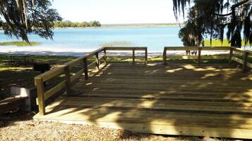 Una terraza de madera que da a un lago, con una mesa de picnic y zona de barbacoa.