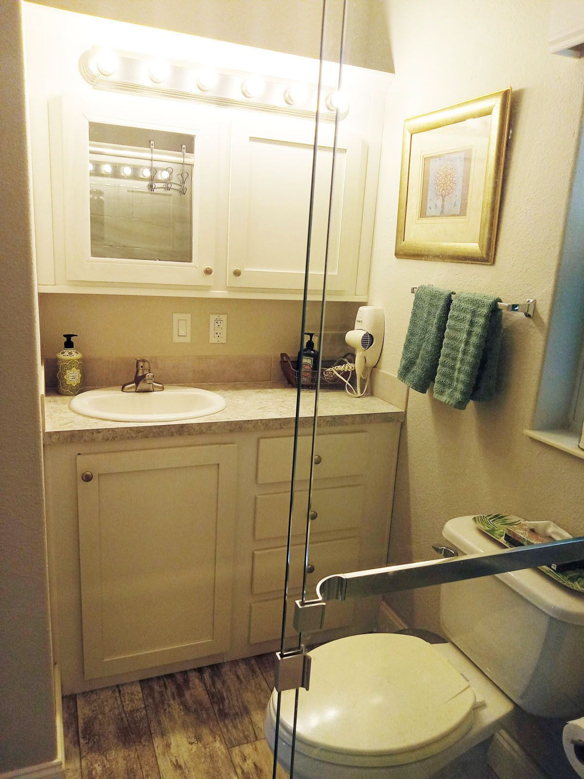Un baño con inodoro, lavabo, tocador y espejo con luces.