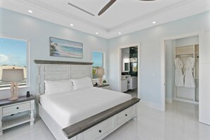 Quarto com cama grande, mesa de cabeceira, luminária, pintura, banheiro com chuveiro envidraçado e closet espaçoso com roupões.