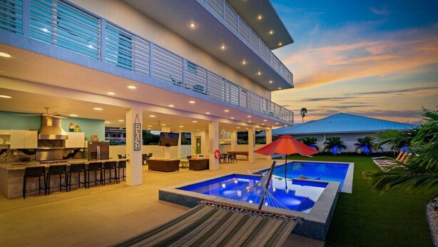 A modern multi-story house with a large outdoor swimming pool, a covered patio, and a kitchen area. - Marathon Sombrero Beach  5 min to Beach, Pool, 70' Dock, Elevator (Marathon)
