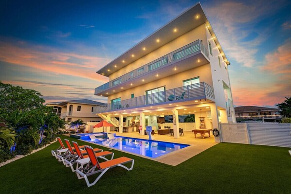 Uma casa moderna com dois andares, piscina, área de estar externa e uma varanda bem iluminada.
