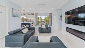 A modern living room with a large flat-screen TV, a fireplace, and a dining area with a view of the outdoors. - Marathon Sombrero Beach  5 min to Beach, Pool, 70' Dock, Elevator (Marathon)