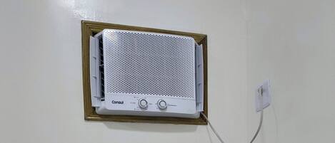 Un equipo de aire acondicionado blanco, fijado a la pared, con un panel de control y un cable de alimentación conectado a un enchufe.