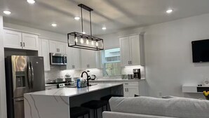 A modern kitchen with white cabinets, stainless steel appliances, a central island, and a grey sofa in the living area. - Luxury home Near NRG, Med Center, Downtown (Houston)