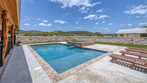 A swimming pool with a stone wall and lounge chairs.