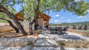 A stone building with a wooden roof, outdoor seating, and a view of hills.
