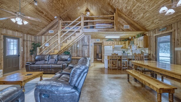 A spacious living area with a leather sofa, wooden benches, and a staircase leading to an upper level.