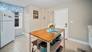 A kitchen with a wooden table, a refrigerator, and a door leading to another room. - Prima Boston North End 2brm (Boston)