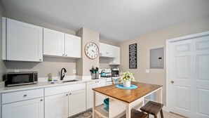 A compact kitchen with white cabinets, a microwave, a kettle, and a clock on the wall. - Prima Boston North End 2brm (Boston)