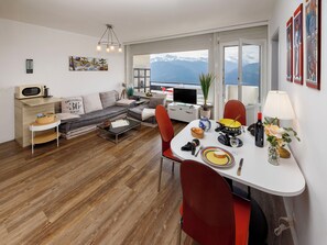 A modern living room with a sofa, dining table, and a view of mountains.