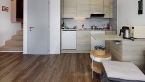 Una cocina compacta equipada con microondas, tostadora y hervidor, un refrigerador pequeño y piso de madera.
