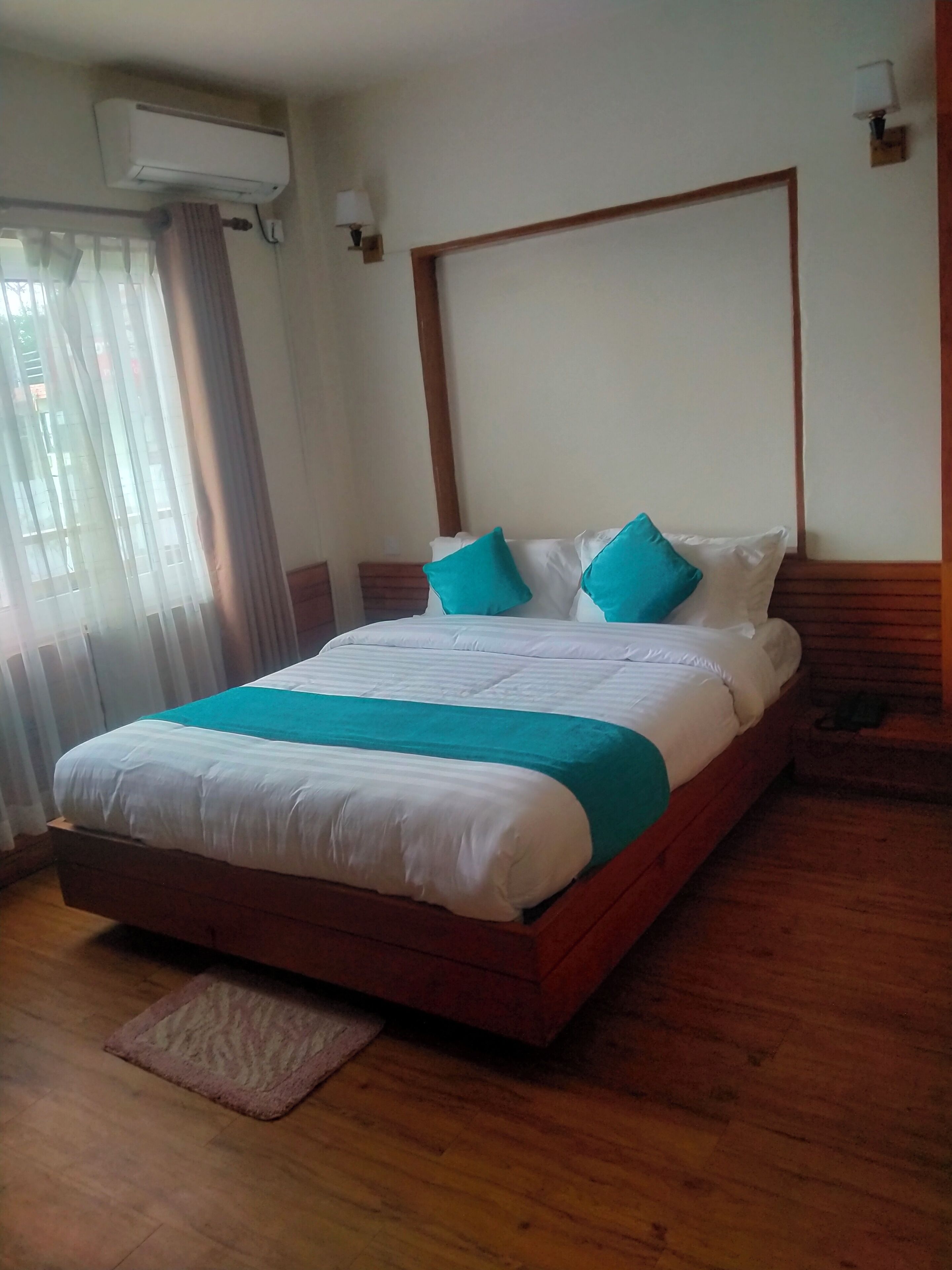 Una cama bien hecha con un cabecero de madera, una manta color turquesa y dos almohadas turquesas.