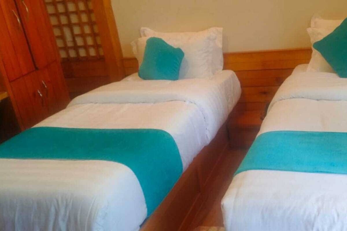 Two single beds with white bedding and teal accents, wooden flooring, and a wooden wardrobe in the background.
