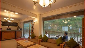A hotel lobby with wooden furniture, a reception desk, and large windows offering a view of the outdoors.