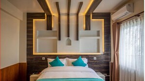 A modern hotel room with a large bed, a nightstand, a built-in shelf, and a ceiling with wooden beams and recessed lighting.