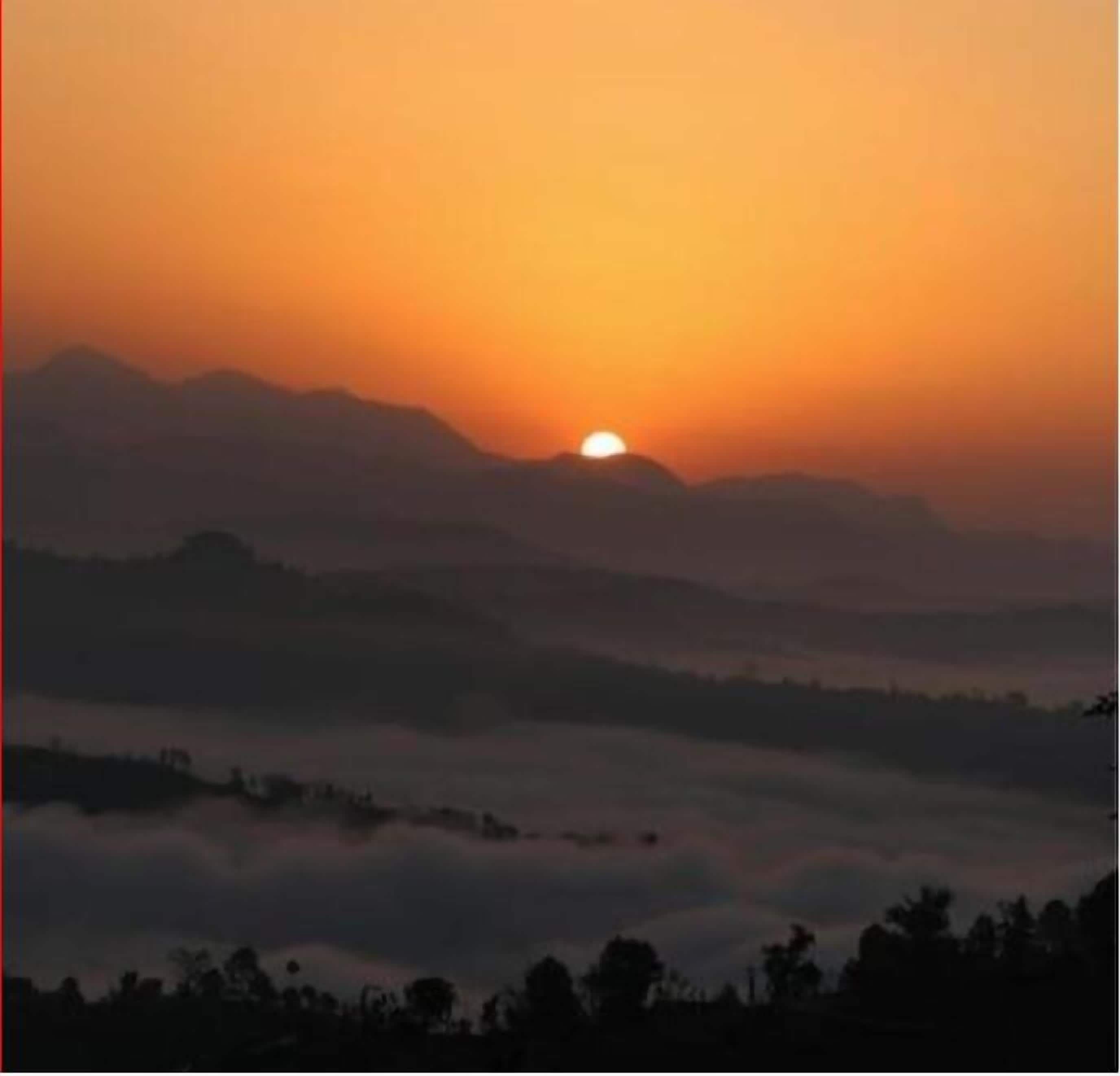 Un amanecer sobre un paisaje montañoso, con vista del sol ascendiendo sobre el horizonte.