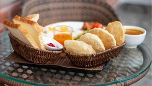 A wicker basket containing bread and a small bowl of sauce on a glass table.