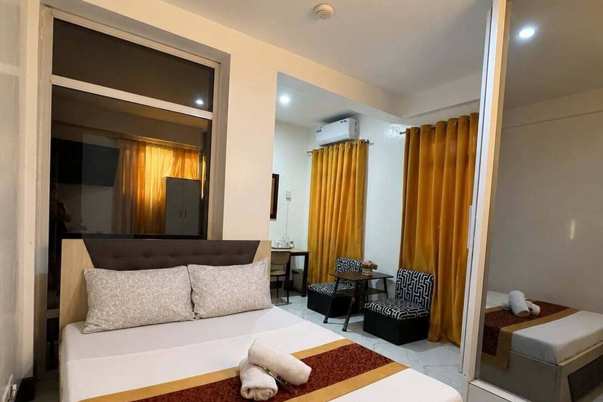 A hotel room with a large bed, a desk, a chair, and a mirror.