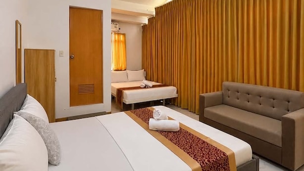 Una habitación de hotel con cama, sofá, camilla de masaje y un amplio ventanal con cortinas.