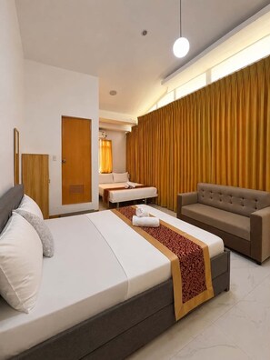 Une chambre d’hôtel équipée d’un lit, d’un canapé, d’une table de massage et d’une grande fenêtre avec des rideaux.