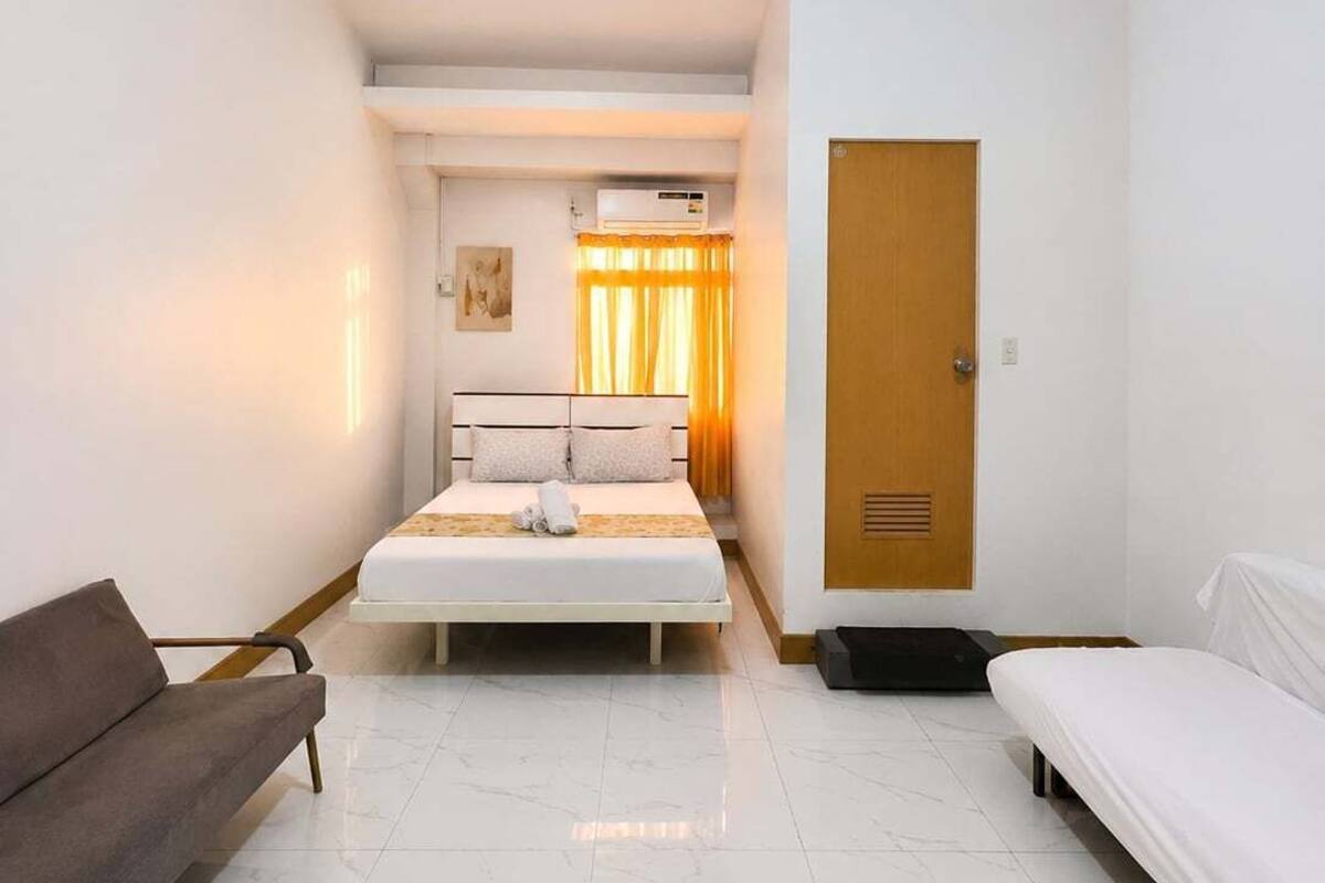 A hotel room with a bed, a sofa, a door, and a ceiling light.