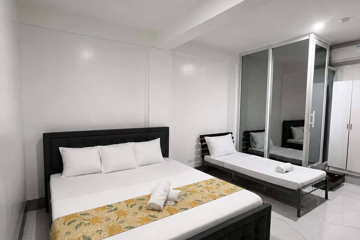 A modern hotel room with a large bed, a bedside table, a walk-in closet, and a mirror.