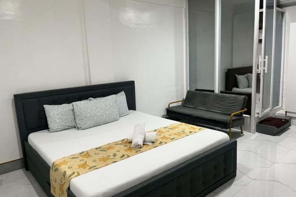 A modern hotel room with a bed, a bench, and a glass door leading to a balcony.