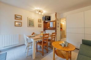 A dining area with a wooden table and chairs, a small round table with cups, and a television mounted on the wall.