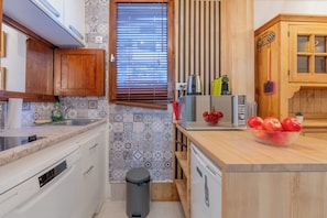 A compact kitchen with wooden cabinets, a built-in microwave, and a small trash bin.