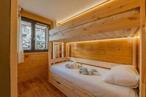 Een slaapkamer met een houten stapelbed, een raam, een nachtkastje en een boek.