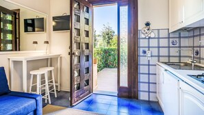 A modern kitchen with a large window, a dining area with a white table and chairs, and a blue sofa. - La Conchiglia by Interhome (Castiglioncello)