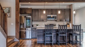 Una cocina moderna con armarios de madera oscura, electrodomésticos de acero inoxidable y una isla central con taburetes de bar.