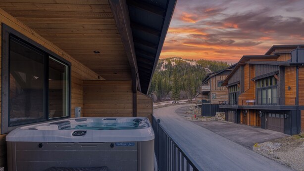 Una cabaña de madera con un jacuzzi en la terraza, con vista a un área boscosa.