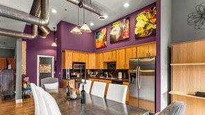 A modern kitchen with wooden cabinets, stainless steel appliances, and a dining area with white chairs. - The 1901 Loft - Heart of Old Colorado City, walking distance to everything (Colorado Springs)