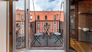 A balcony with a table and two chairs, a potted plant, and a view of a brick building. - The 1901 Loft - Heart of Old Colorado City, walking distance to everything (Colorado Springs)